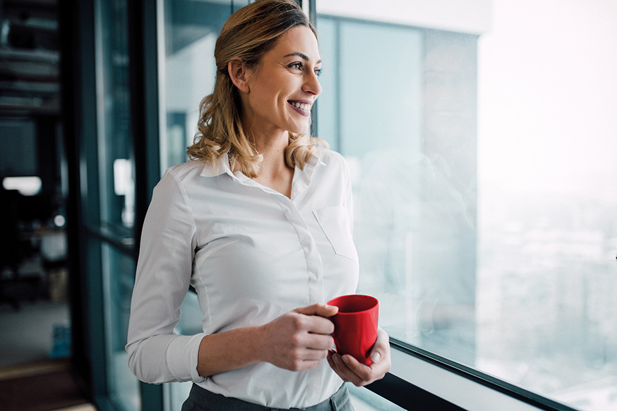 Image of a lady holding a red mug and staring out of the window.